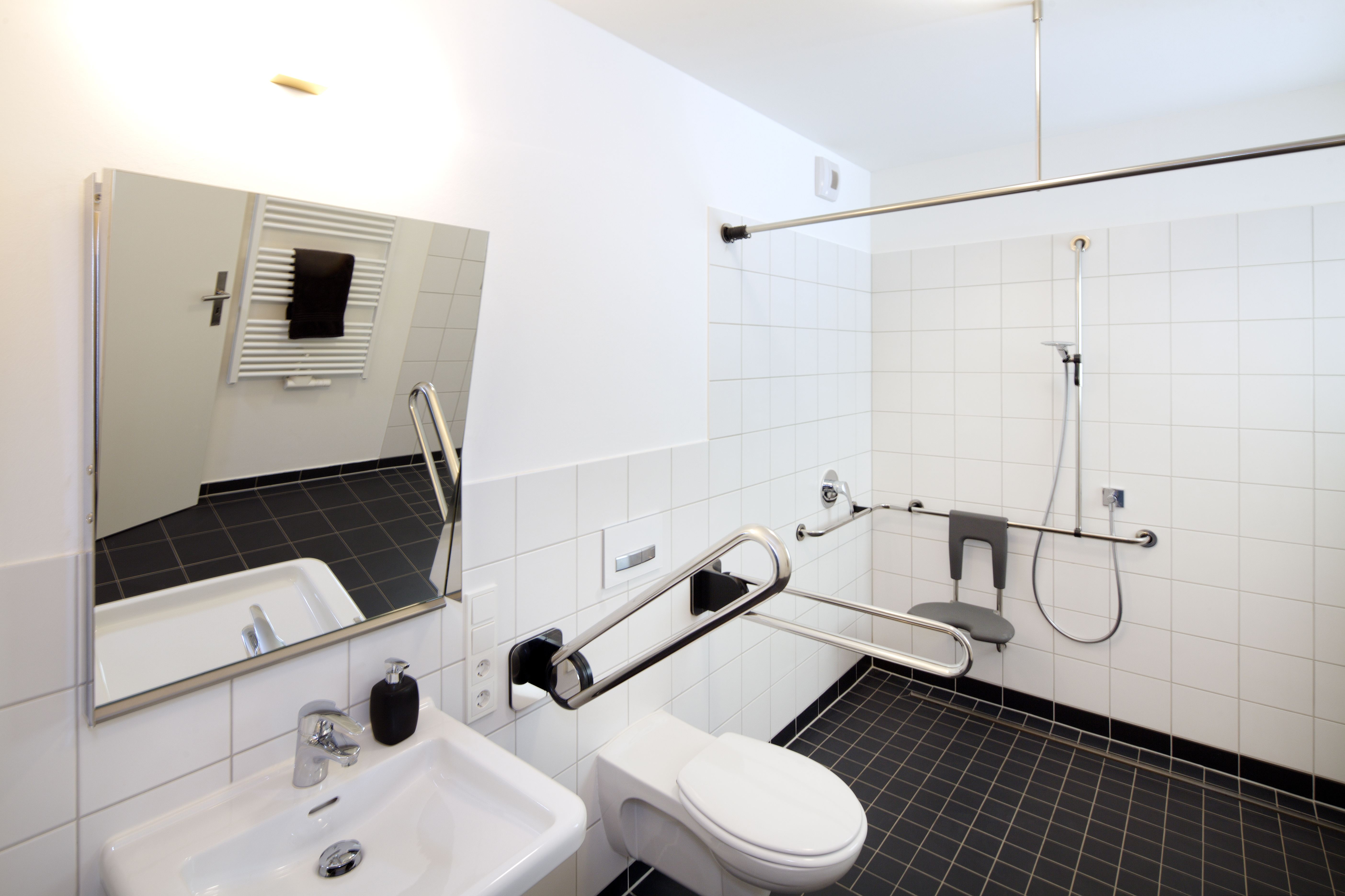 Barrierefreies Bad mit klappbaren Haltegriffen am WC und bodengleicher Dusche mit Klappsitz
