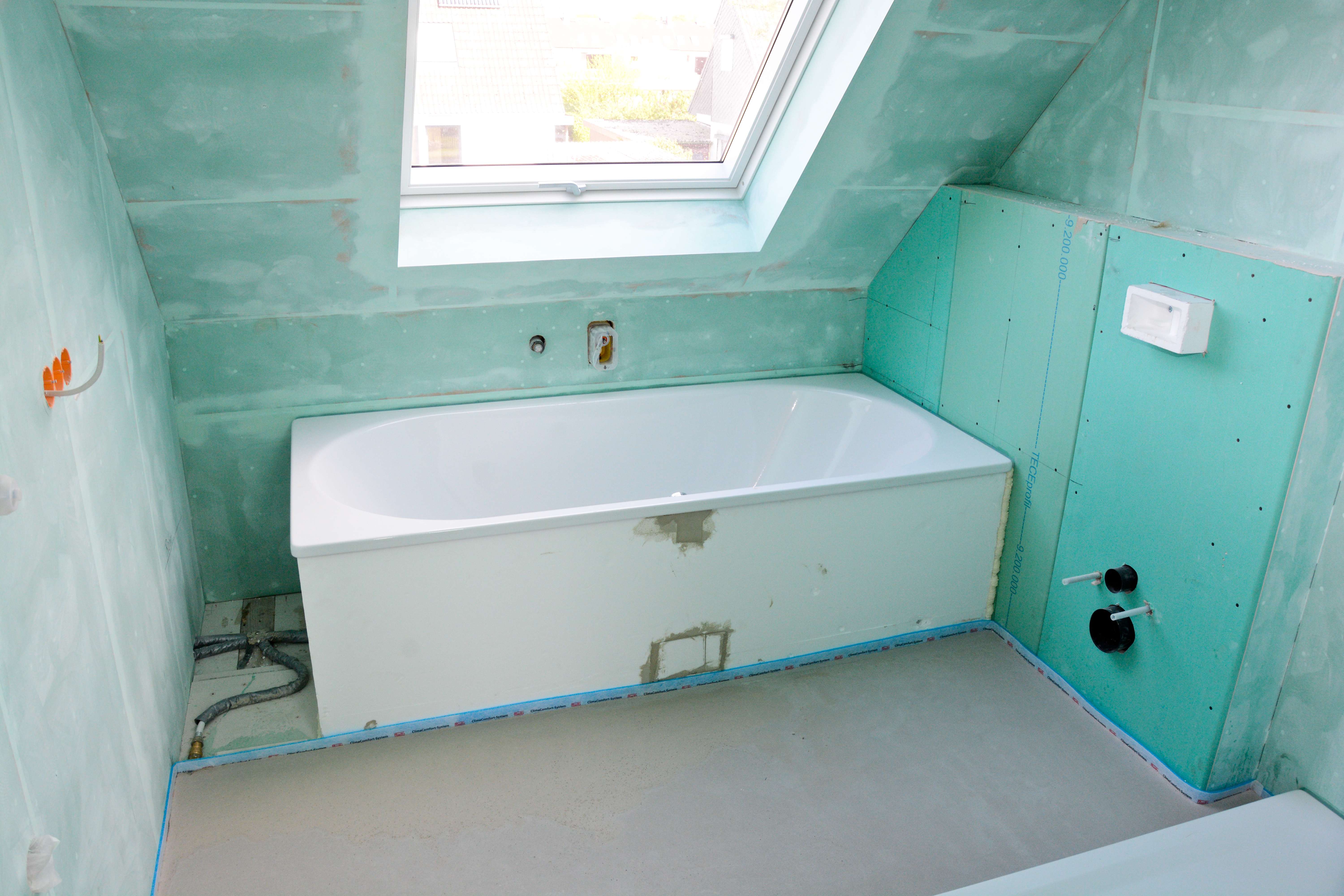 Badezimmer während der Sanierung mit Feuchtraumplatten, eingebauter Wanne und freiliegenden Leitungen